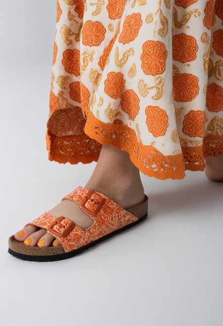 1girl, solo, simple_background, white_background, birksonfeet, orange_toenail_polish, close-up, lower_body, footwear_focus, patterned, long_skirt