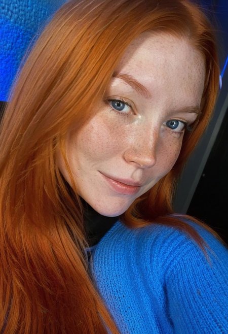 fair skin with freckles, long hair, very long hair, long straight orange hair with a reddish tint, straight hairstyle, cool artificial lighting, wearing a bright blue knit sweater, bright blue eyes, medium-length brown hair, wearing a black high-neck sweater, light smile with a hint of contemplation.