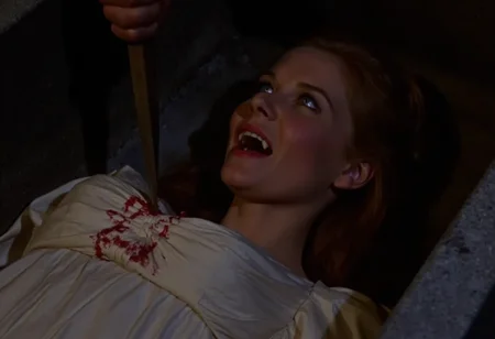 full body shot of a young vampire woman lying in a coffin, a hand is aiming a stake at her chest from off-screen , screaming showing fangs, pale skin, dark eyes, open blue eyes staring at viewer, blood running from the corners of her mouth, wearing a conservative white victorian silk gown. Soft warm light at night   <lora:hammer-000073:1>