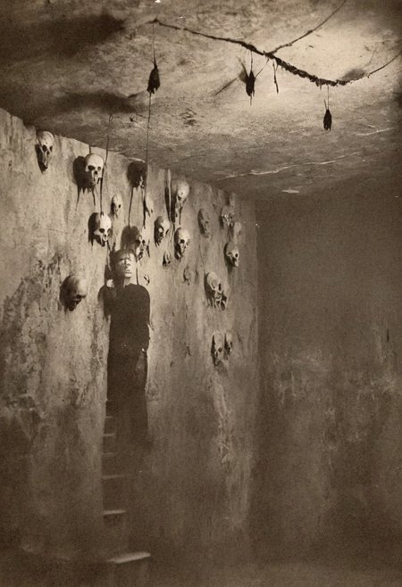 <lora Sairento Hiru style:0.8>, antique photo, eerie atmosphere, creepy man, cave, descent into madness, lovecraft horror, walls made of skulls, one bat hanging from the ceiling, <lora:Antique_Photo:1.2>