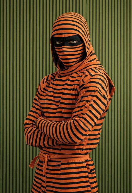bw-grignani, emphasis lines, Capture the essence of illusion: A orange ninja clad in striped shinobi attire, poised before a red/green striped wall. Explore how the ninja seamlessly blends into the pattern of thick, perfectly aligned stripes, merging with the illusion of infinite lines.