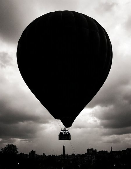 High-contrast black and white photograph, a colossal hot air balloon silhouetted against a stormy Parisian sky, intricate basket details visible, dramatic lighting, shallow depth of field, Canon EOS 5D Mark IV, 85mm lens, f/2.8, ISO 400.