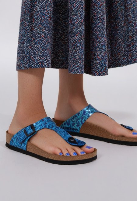 1girl, solo, dynamic_pose, simple_background, white_background, gizehonfeet, blue_toenail_polish, close-up, lower_body, footwear_focus, patterned, long_skirt