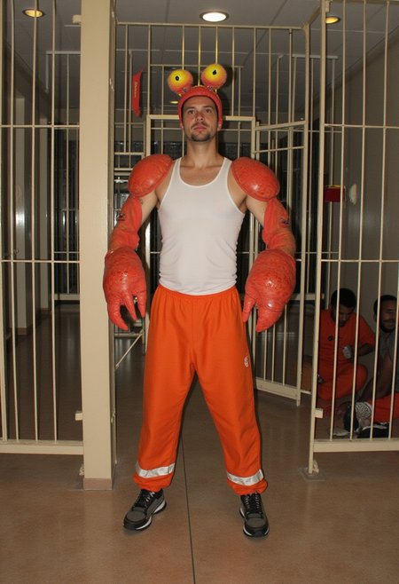 Photo of a one man wearing crab costume. He has crab head and claws. He wears orange prison uniform an white top tank. 
Futuristic diselpunk prison. Few male prisoners sitting on the floor.
Dynamic scene. Film grain. Intricate details.