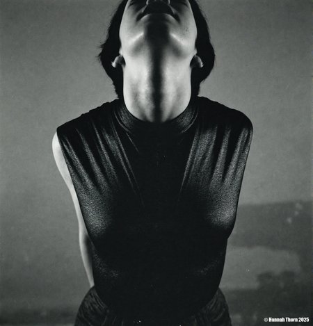 A black and white photo from a frontal camera angle, featuring a  mannequin wearing a sleeveless, textured black top, positioned in the middle of the frame. the woman, who appears to be in her mid-twenties, has short, dark hair and a slim, muscular physique. she is facing the viewer, with her eyes closed and her mouth slightly open, as if she is in a state of contemplation. the background is a plain, muted grey wall, and the lighting is soft and diffused, casting shadows that accentuate the  woman's face and upper body. the overall mood of the image is somber and unsettling, with a focus on the figure's facial features and clothing.<lora:_Flux\Saul_Leiter_BW.safetensors:1.0:1.0>