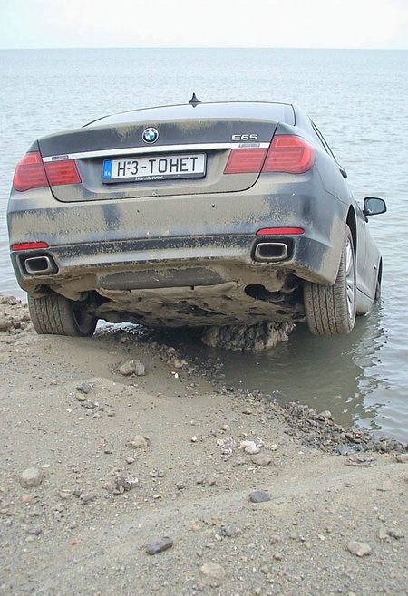 d1g1cam. 
a photo taken from uphill of a dirty and worn vehicle, a visually damaged and slightly deformed 2009 BMW 7 E65 sedan with it's rear half dipped into the sea and the front half is tilted against seashore. Car is dirty with very thick layer of moist dust from below. Car is tilted upwards with front bumper above the water, but rear half of the car hidden under water surface. Cropped peek of bland ground cliff below the picture. Horizontal russian license plate with text "H3 T0HET".
<lora:Digicam:0.7>