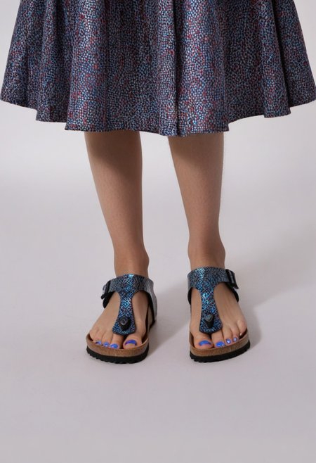 1girl, solo, dynamic_pose, simple_background, white_background, gizehonfeet, blue_toenail_polish, close-up, lower_body, footwear_focus, patterned, long_skirt