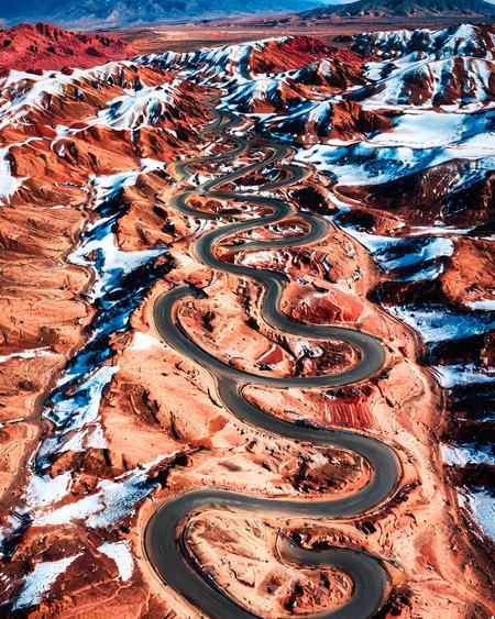 vertical perspective aerial photography, desert_road, red_rock_terrain, undulating_hills, clear_skies,  travel car on road,  <lora:sky:0.8>