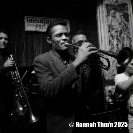 A  captivating single black and white photograph, reminiscent of a Dorothea Lange portrait fused with a  gritty Henri Cartier-Bresson street scene, depicts a jazz band performance in  a dimly lit New Orleans club.  The central figure, a middle-aged Black man playing trombone with eyes closed, embodies the relaxed intensity of a Louis Armstrong  performance, bathed in chiaroscuro lighting à la Rembrandt.  To his right, a blurry, almost impressionistic bassist and a sharply focused trumpeter (a  close-up worthy of a Diane Arbus study, showcasing the strain of intense focus) complete the ensemble.  The background, suggesting depth through selective focus and atmospheric perspective, features "The Spotted Music Club" sign and street glimpses, creating  a nostalgic mood akin to a Walker Evans photograph.  The grainy texture mimics vintage silver gelatin prints, while the overall composition evokes a powerful narrative through light and shadow. <lora:_Flux\Vintage_Jazz-Club.safetensors:0.7000000000000001:0.7000000000000001> <lora:_Flux\_Characters\Chet_Baker_old.safetensors:1.0:1.0>
