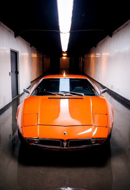 gleaming orange Maserati Bora, symmetrical front view, wet tunnel reflections, bright headlights, neon lights, 4K, highly detailed, ((grainy 35mm photo))