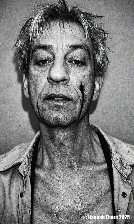 A black and white portrait of a middle-aged man with short, messy hair and a serious expression. he appears to be in his late 60s or early 70s, with light skin and a slightly wrinkled face. his eyes are closed, and he is looking directly at the camera. his hair is messy and unkempt, with some strands falling down his back. he has a black shirt draped over his shoulders, and there are scars on his face and neck, suggesting he has been involved in a serious or intense situation. the background is a plain, textured wall, and the lighting is dramatic, casting shadows on the man's face and upper body. the overall mood of the image is somber and contemplative.<lora:_Flux\Anders_Petersen.safetensors:1.0:1.0>