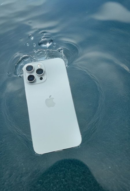 A smartphone with water ripples on its surface and a water droplet suspended above it, against a gradient blue background, suggesting a tranquil and clean environment.
