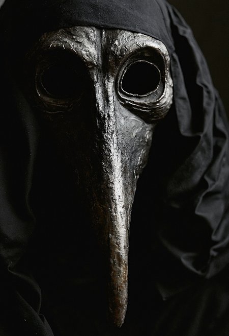 drk4rt photo, closeup of a plague doctor's mask made out of paper mache, long beak, glossy black paint, the image is very dark, analog film, grainy, macabre, fascinating photography, 35mm