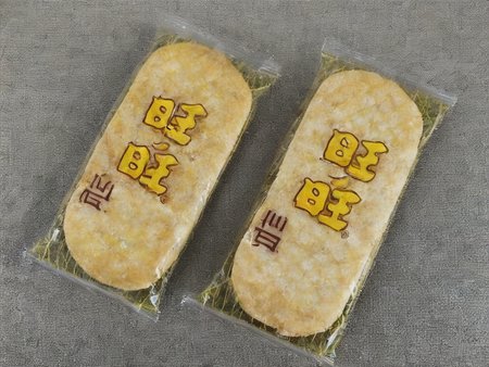 A street vendor's cart brimming with senbei (Japanese rice crackers). The cart is positioned on a sidewalk, with neatly stacked senbei packets or trays, showcasing the product in abundance. The scene should be as realistic as a high-resolution photograph, capturing the hustle and bustle of street life in the background, but with the focus primarily on the cart and its contents. The lighting should be natural, highlighting the details and textures of the senbei,  <lora:senbei:0.85>