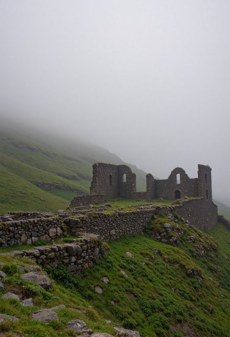 A misty morning scene, showcasing the ruins of a stone structure nestled atop a verdant hill. Low-lying fog drifts across the lush green landscape, creating an ethereal atmosphere. The stone walls are weathered and partially collapsed, hinting at age and history. The overall lighting is soft and diffused, emphasizing the moody and mysterious mood. The style should be photorealistic, with a focus on detail and depth of field. The color palette consists primarily of greens, grays, and muted browns. <lora:VividlySurrealOrigin:0.6> <lora:FluxDFaeTasticDetails:0.6> <lora:42lux-UltimateAtHome-flux-highresfix:0.25>