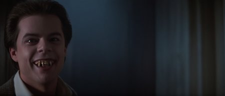 cinematic film still of  <lora:Fright Night 1985 style v2:1>
In the 1980's vampire human Evil Ed Stephen Geoffreys,19yo vampire with white vampire teeth,Vampire7,white makeup a man with a creepy smile on his face,solo,smile,short hair,open mouth,black hair,1boy,male focus,teeth,indoors,blurry,blurry background,facial hair,fangs,portrait,realistic , horror themed, dark themed, low key light, dramatic light, dramatic shadow light, contrast, cinematic color, cinematic look, filmic, realistic, realism, perfection, perfect, Kodak, Kodak film, movie still, Fright Night 1985 style, Fright Night Film style, shallow depth of field, vignette, highly detailed, high budget, bokeh, cinemascope, moody, epic, gorgeous, film grain, grainy