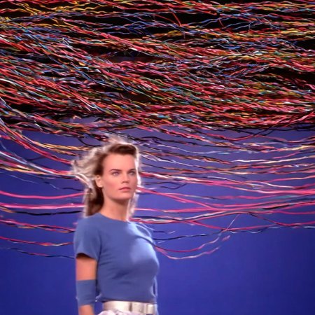 70mm shot on sony analog HDTV camera laserdisc style dorky australian brunette woman in standing in large room with cables on floor like television studio wide shot surrounded by swirling colour and sexy smirking at camera with a little wink. background is 1990s japanese beauty scenes exploding televisions electricity in background in a surreal fashion technology moving into her head cables and wires low contrast super sharp imagery