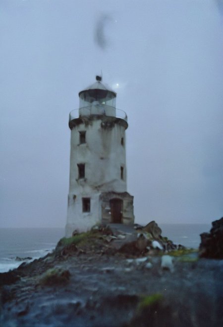c41_hasselblad_portra400, In a grainy, handheld video, a lone explorer investigates an old, decrepit lighthouse on a foggy night. As he ascends the spiral staircase, strange whispers and ghostly moans fill the air. At the top, he encounters a monstrous, ethereal being with tentacles and multiple glowing eyes. The footage is chaotic and filled with static, capturing the explorer's terror and the creature's unearthly presence.