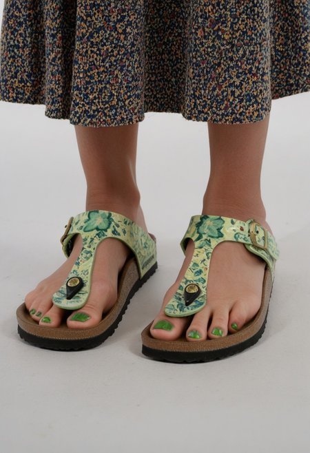 photograph of woman's feet wearing sandals, 1girl, solo, dynamic_pose, simple_background, white_background, gizehonfeet, (green toenail_polish), (close-up:0.5), lower_body, footwear_focus, patterned long_skirt
