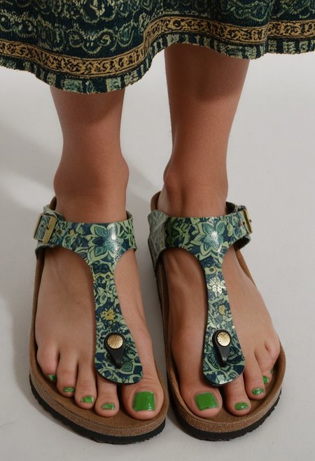 photograph of woman's feet wearing sandals, 1girl, solo, dynamic_pose, simple_background, white_background, gizehonfeet, (green toenail_polish), (close-up:0.5), lower_body, footwear_focus, patterned long_skirt