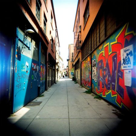 Shot with a Holga camera, an urban alleyway filled with graffiti, soft light filtering from above, and a surreal vignette highlighting the vibrant yet slightly desaturated colors.