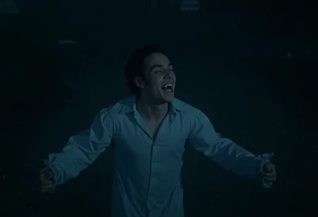 medium shot of a young vampire man standing on a cemetary in the rain at night, wearing a victorian nightshirt, arms spread, looking up with eyes closed, smiling showing fangs, pale skin, taken from above. low light at night <lora:hammer-000073:1>
