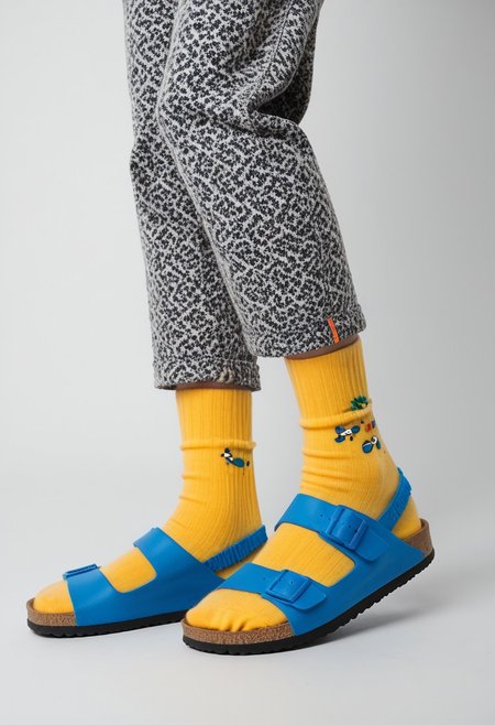 (photograph of woman's feet wearing socks and sandals and leggings), 1girl, solo, dynamic_pose, simple_background, white_background, scksnsndls, patterned blue and yellow socks, lower_body, footwear_focus, ankles, calves, birksonsocks, birkenstock