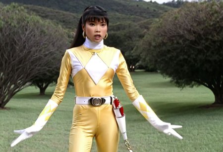 Trini Kwan, alone, long black straight ponytail hair, fringe, bangs, it's morphin time, helmetless, yellow power ranger, uniform, yellow catsuit, white turtleneck collar, white gloves boots belt, red holstered weapon, neutral facial expression, large chunky steel hoop earrings, in action, facing camera, looking at viewer