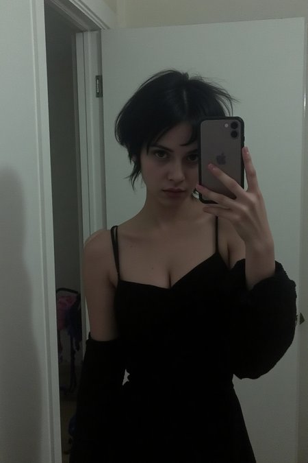 A 23-year-old goth petite woman stands in front of a foggy mirror, her short black hair framing her pale face. In a black bare shoulders dress, she snaps a moody selfie on the bathroom mirror, dirty mirror, her eyes downcast but still rebellious