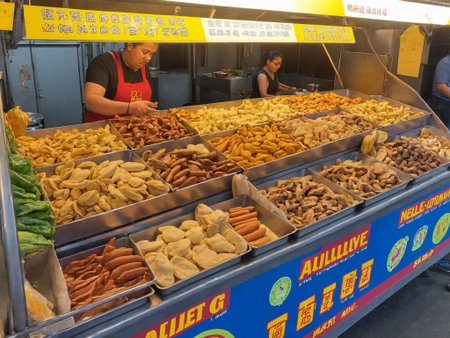 buffet,A street food , set up along a bustling sidewalk. She is actively preparing or serving food, her appearance reflecting both professionalism and beauty. The colorful and inviting stall displays a variety of local delicacies. Steam or smoke rises from the cooking equipment, adding to the ambiance. The background captures the lively street scene with pedestrians showing interest in the food. The scene should be as realistic as a high-resolution photograph, with natural lighting that highlights the vibrant colors and textures of the food, the authenticity of the street setting, and the allure of the vendor,   <lora:t9m:0.75>,night market,
