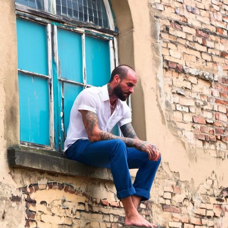 urban, tattooed man, detailed skin, two arms resting on knee, sitting on edge of stone windowsill, beam, under window, perched, handwriting graffiti, detailed, plaster, window frame, bokeh background, blue trousers, white short-sleeved shirt, both hands, highly-detailed face, stubble, individual hairs, sideburns, neck, brick wall, cyan, window hole with metal grid, photorealistic, barefoot, submerged, high quality