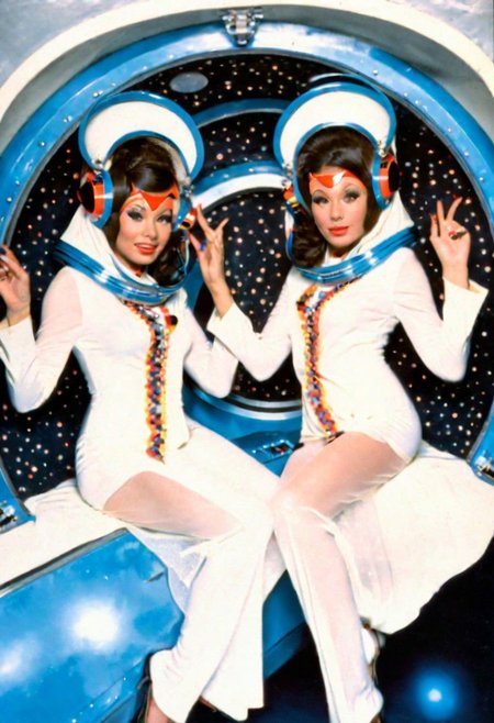 conceptual portrait, sexy twin temple brunette pin-up priestess aboard the sexy futuristic spacecraft, floating playfully in zero gravity, dynamic pose, 1970s sexploitation sci-fi film, pulp-sf, weird future fashion, headdress, plastic, veil, mask, helmet