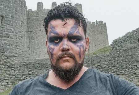 4RIEL, male viking, short beard, dusty background, in front of a castle, daylight, dramatic, face paint, 35mm film photography