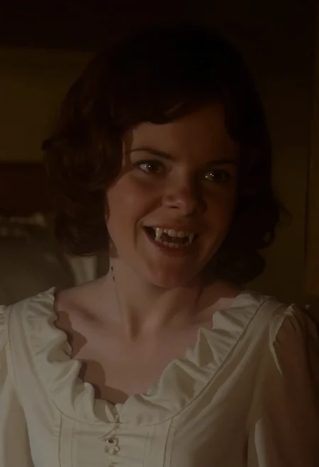close-up face shot of a young vampire woman standing in a victorian bedroom, head tilted to side prominently showing bite marks on the side of her throat, wearing a conservative victorian white nightgown, high neckline, pale skin, smiling showing fangs. Soft warm light at night  <lora:hammer-000073:1>