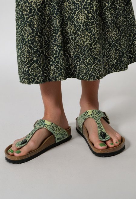 photograph of woman's feet wearing sandals, 1girl, solo, dynamic_pose, simple_background, white_background, gizehonfeet, (green toenail_polish), (close-up:0.5), lower_body, footwear_focus, patterned long_skirt
