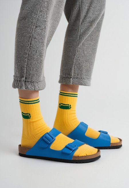 (photograph of woman's feet wearing socks and sandals and leggings), 1girl, solo, dynamic_pose, simple_background, white_background, scksnsndls, patterned blue and yellow socks, lower_body, footwear_focus, ankles, calves, birksonsocks, birkenstock