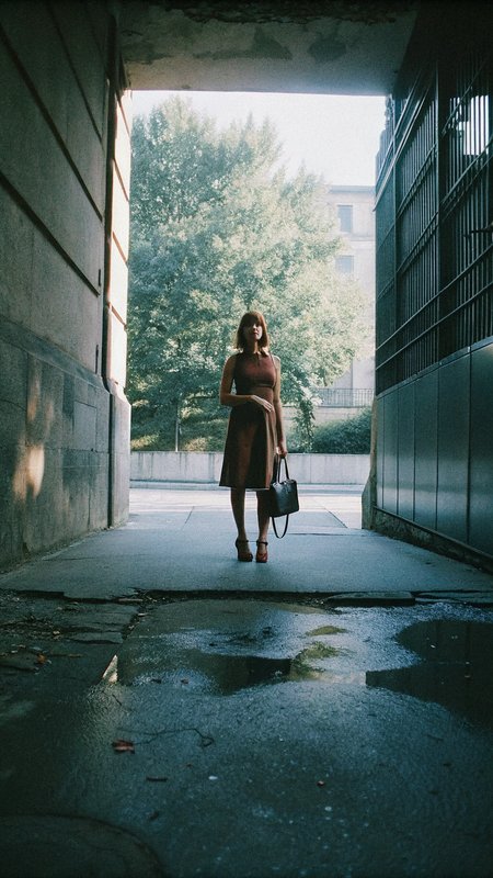 A 28-year-old slim European woman stands confidently in a stylish brown dress. Urban background, soft natural lighting, elegant heels, minimalistic jewelry, and leather handbag complete her look. standing at full height, full-body shot, head-to-toe view, entire outfit visible 